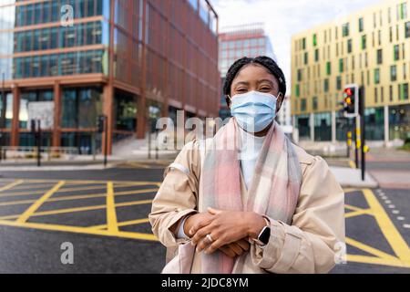 Woman with face covering facing camera in town centre with main road in background Stock Photo