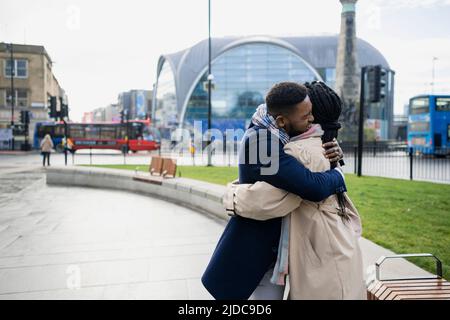 Couple hugging with arms around each other in town Stock Photo