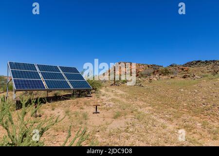 Isolated dry semi desert area with rocks and grassy sandy areas.  Nine solar panels mounted on a metal frame to provide electricity. Stock Photo