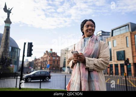 Woman with mobile smiling and looking away with road in background Stock Photo
