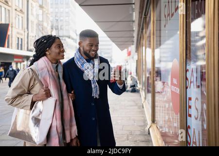 Cheerful couple window shopping and checking mobile phone, smiling and looking through store window Stock Photo