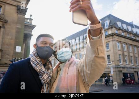 Couple in town with face coverings taking selfies on mobile phone Stock Photo