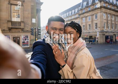 Cheerful couple in town taking selfie with mobile phone, woman with hand on man's chest Stock Photo