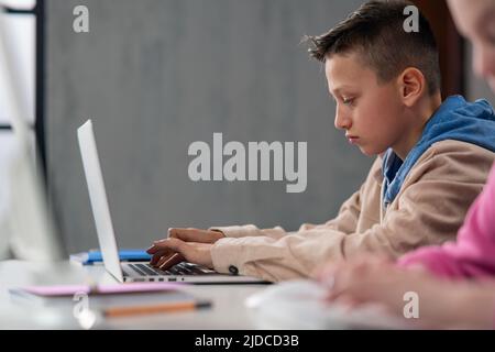Side view of schoolboy using computer in classroom at school Stock Photo
