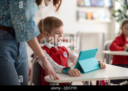 Happy schoolboy using digital tablet during lesson in classroom at primary school. Stock Photo