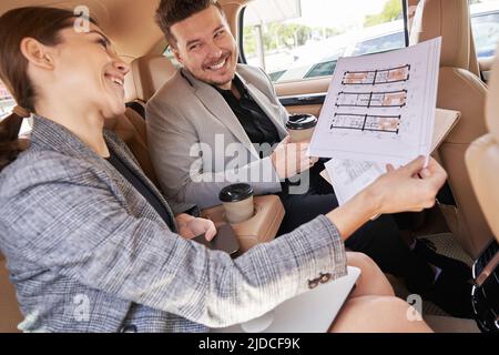 Cheerful man and woman discussing architectural plan in car Stock Photo