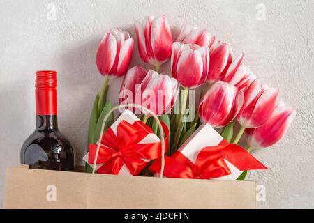 Mother's Day or Women's Day, birthday, wedding congratulation. Spring tulips with a gift box and a bottle of wine in a paper bag. Stock Photo