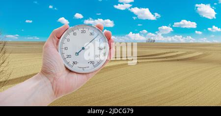A hand holding thermometer in nature agriculture field background against a cloudy sky