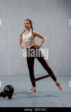 Sports woman in fashion sportswear exercising with elastic band stretch over greay background. Stock Photo