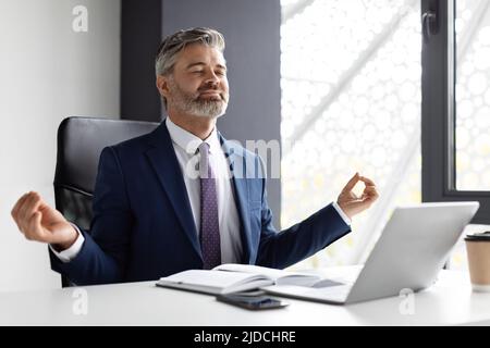 Portrait Of Relaxed Middle Aged Businessman Meditating At Workplace In Office Stock Photo