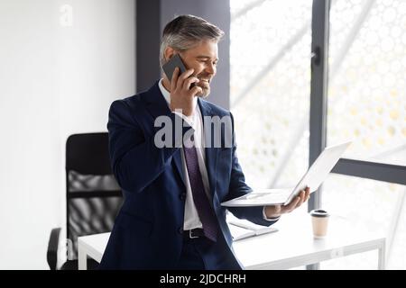 Middle Aged Businessman Talking On Cellphone And Using Laptop At Office Stock Photo