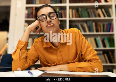 Tired female student sleeping on table in front of laptop, studying online or preparing for exams in library Stock Photo