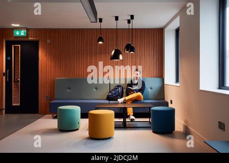 Student reading in sofa in student accommodation leisure space, halls of residence. Duke Street Riverside - Norwich University of the Arts, Norwich, U Stock Photo
