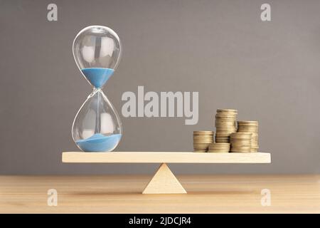 Balance Between Time and money concept. Sand clock and stacked coins on Seesaw. Copy space Stock Photo