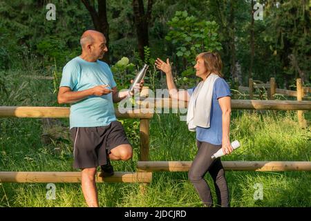 Male mature adult offering water to his workout couple in the middle of the nature in the city park Stock Photo