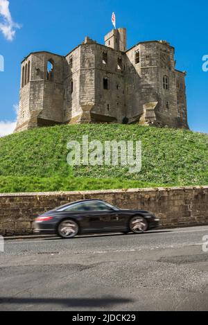 Car travel, view in summer of a sports car speeding past a ruined medieval castle in the English countryside, Warkworth, Northumberland, UK Stock Photo