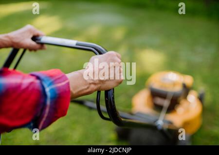 Close-up of elderly woman mowing grass with lawn mower in the garden, garden work concept. Stock Photo