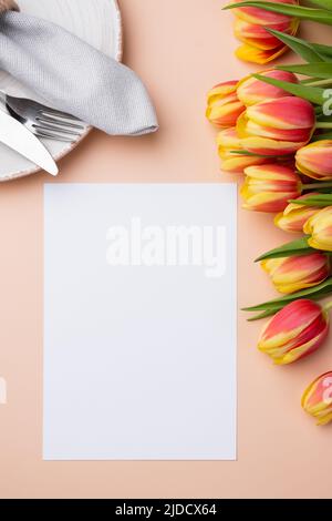 Mock up menu card. Top view of table setting with menu card, cutlery and fresh tulips for festive dinner Stock Photo