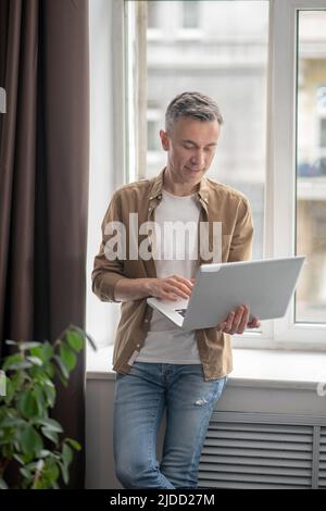 Man standing with back to window working on laptop Stock Photo
