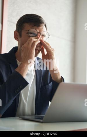 Man in office experiencing exhaustion and rubbing his nose Stock Photo
