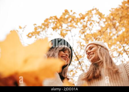 Two young happy women against background of autumn sky and yellow trees . Leaf fall. Positive emotions. Female friendship. Student times. Autumn mood Stock Photo