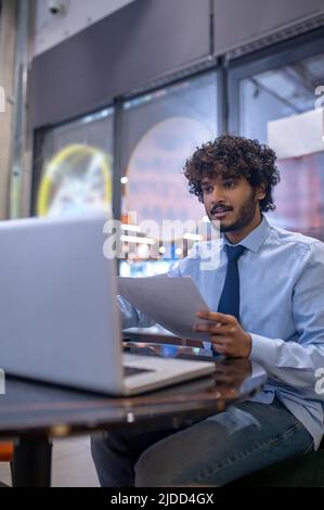 Man with papers looking at laptop sitting at table Stock Photo