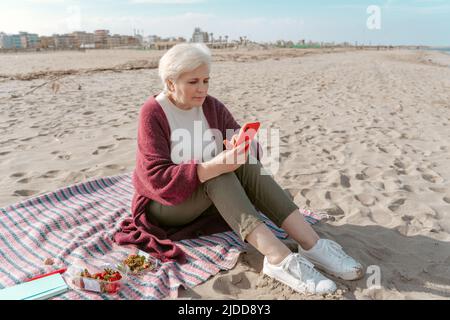 Senior woman with the cellphone on the beach Stock Photo