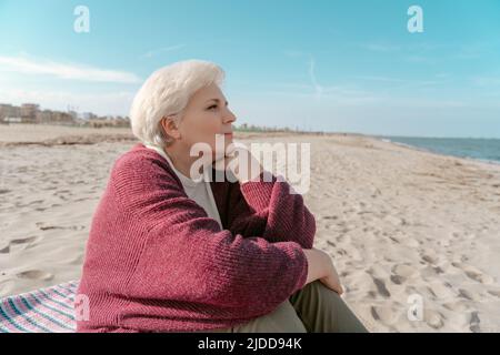 Thoughtful senior woman seated on the beach Stock Photo