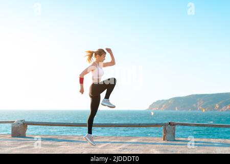 Young fit woman jumping high on beach with sunset, active caucasian young adult female workout with , bodyweight training exercise for woman, self mot Stock Photo