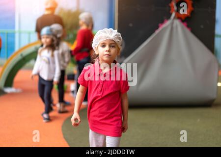 Cute little girl climber dressed protective hat before dress up helmet standing in climber centre amusement park for children. Caucasian female climbe Stock Photo