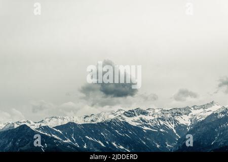 single dark cloud against clear sky, abstract photography, concept, single lonely cloud over snow peaks mountain. Stock Photo