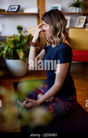 A yogi woman is sitting on a yoga mat in the lotus position and doing breathing exercises. Stock Photo