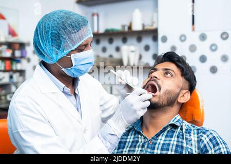 dentist with surgical gloves and face mask checking teeth of patient at hospital or clinic - concept of oral care, hygienist and professional Stock Photo