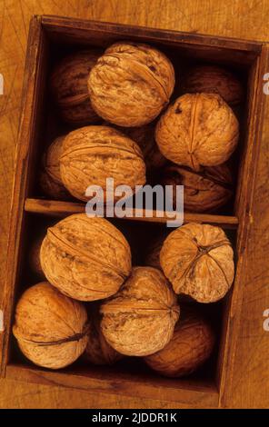 Close up from above of walnuts in their shells lying in compartmentalised wooden box Stock Photo