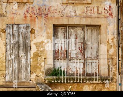 An old shop window with faded red lettering is closed in the town of Menerbes in the Luberon area of France. Stock Photo