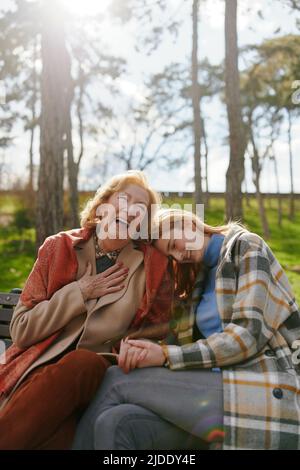 A grandmother is laughing and having fun with her adolescent granddaughter while sitting on the park bench. Stock Photo