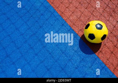 Colorful sports court background. Top view light blue field rubber ground with shadow from football goal net and yellow soccer ball on sunny day Stock Photo
