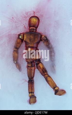 Dark stained wooden mannequin lying face down in ice and surrounded by blood Stock Photo
