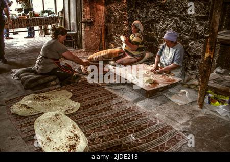 Lusakert, Armenia, May 14, 2022.: A woman sitting on the floor takes out a thin sheet of baked fragrant lavash from a red-hot oven in the floor. Stock Photo
