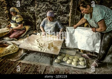 Lusakert, Armenia, May 14, 2022.:Baking bread-pita bread, one woman distributes the dough in portions, the other rolls it into thin sheets,the third p Stock Photo