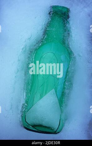 Green glass beer bottle shattered by ice lying in block of ice Stock Photo