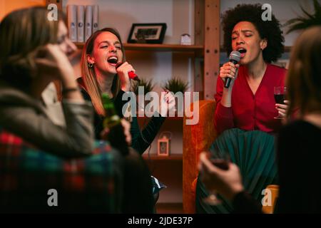 Happy multiracial friends are sitting at home and having fun on karaoke night. Stock Photo
