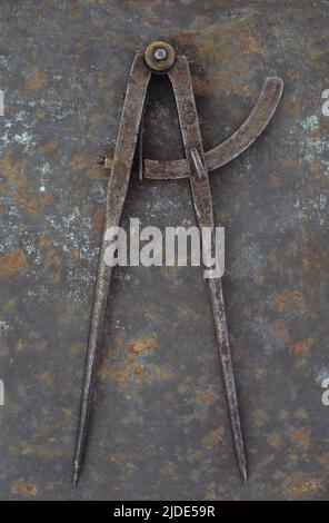 Pair of vintage tarnished measuring dividers or compasses lying on rusty metal sheet Stock Photo