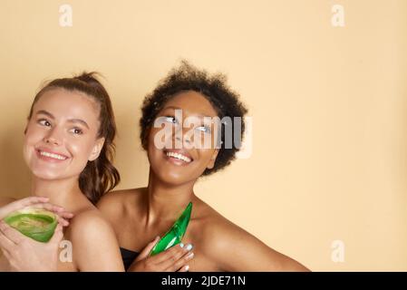 Body and face skin care. Smiling african american and caucasian female models with aloe moisturizing gel and perfect hydrated soft skin Stock Photo