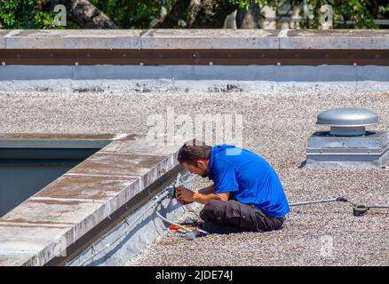 NEW ORLEANS, LA, USA - JUNE 16, 2022: Electrician working on rooftop of bank building from a sitting position Stock Photo