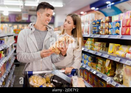 Young loving couple making purchases together, choosing cookies in grocery store Stock Photo
