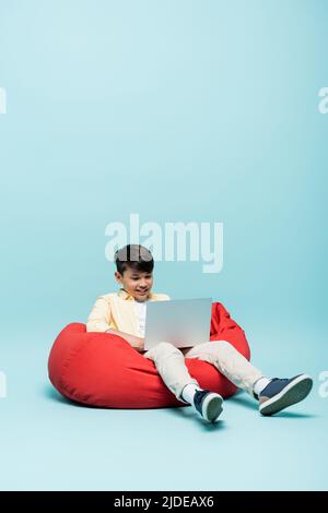 Smiling asian schoolboy using laptop on blue background Stock Photo