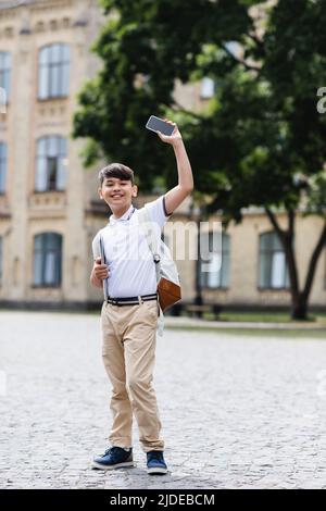 Positive asian schoolkid holding laptop and smartphone outdoors Stock Photo