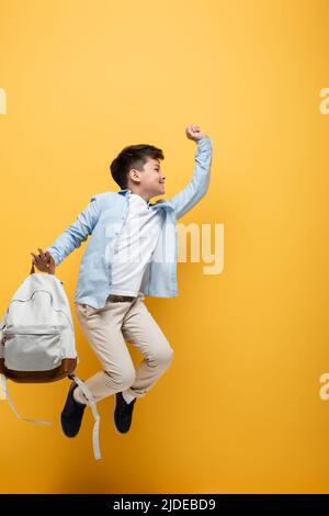 Happy schoolboy with backpack jumping on brown background Stock Photo ...