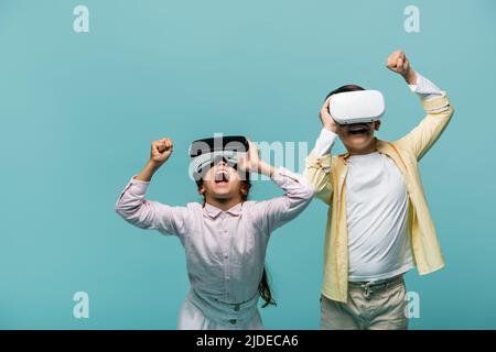 Excited preteen friends using vr headsets isolated on blue Stock Photo